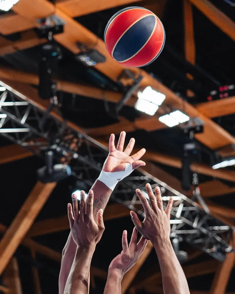 Mains de basketteurs tendues vers le ballon sous les projecteurs