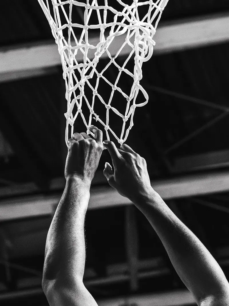 Mains d'un basketteur accrochées au filet du panier, en noir et blanc